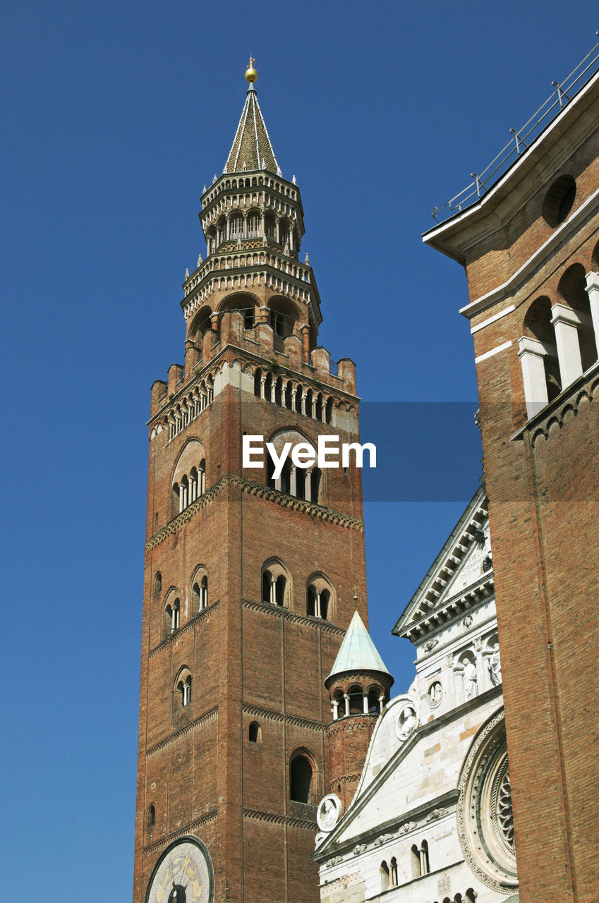 LOW ANGLE VIEW OF CLOCK TOWER AMIDST BUILDINGS AGAINST CLEAR SKY