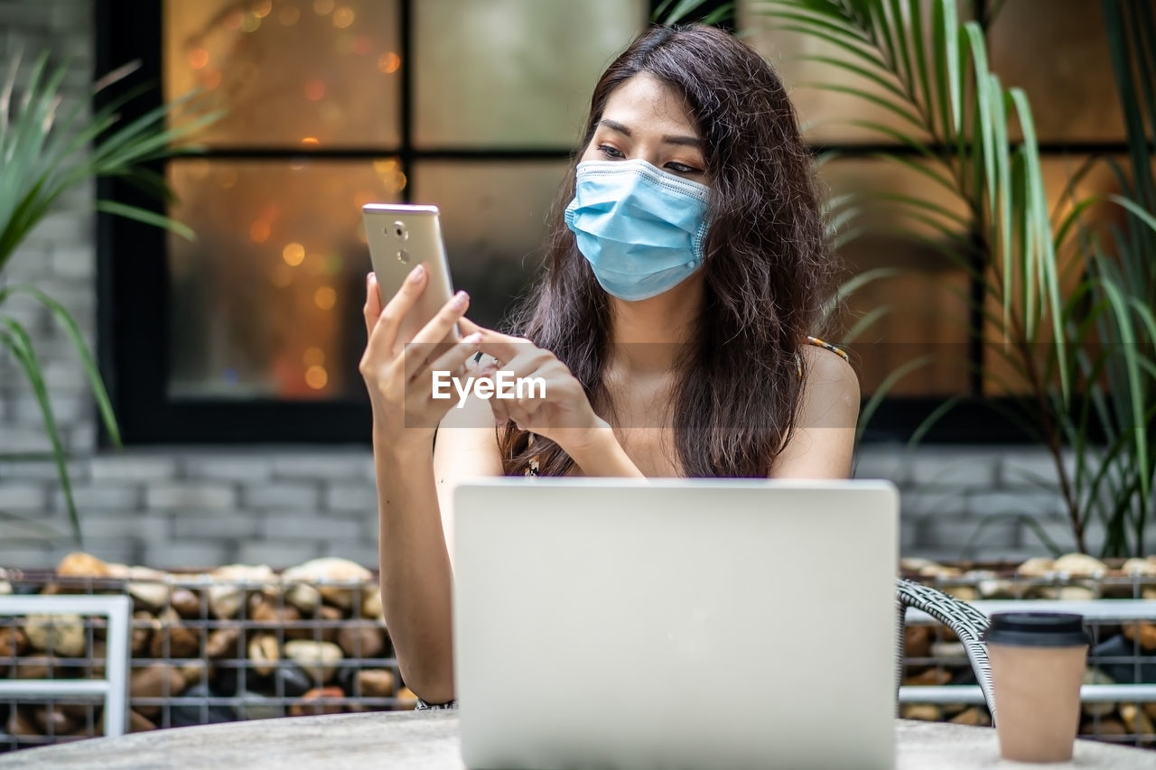 Young woman wearing mask while using phone at cafe