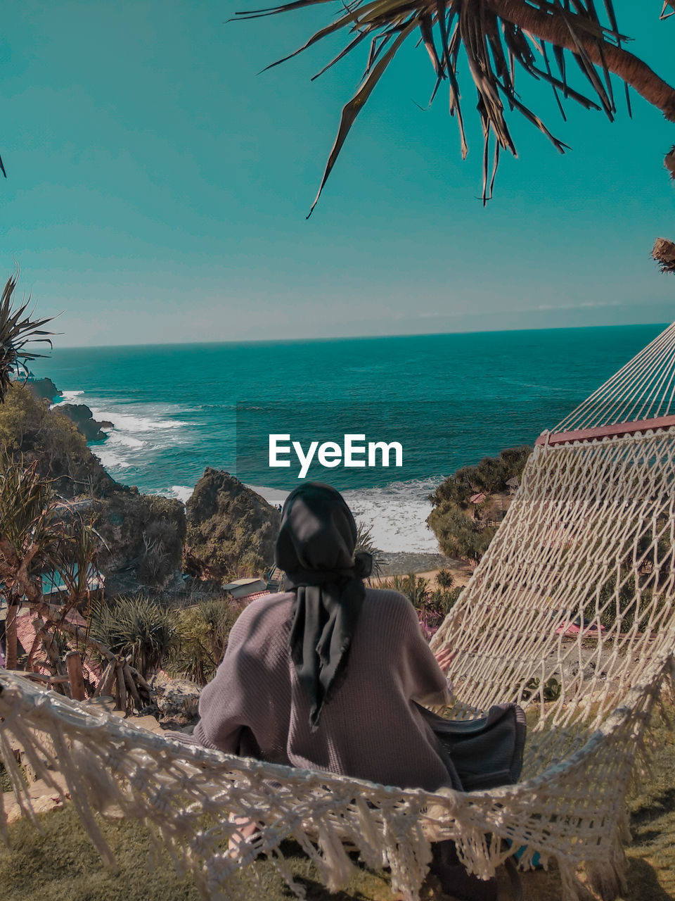 Rear view of woman sitting on hammock against sea