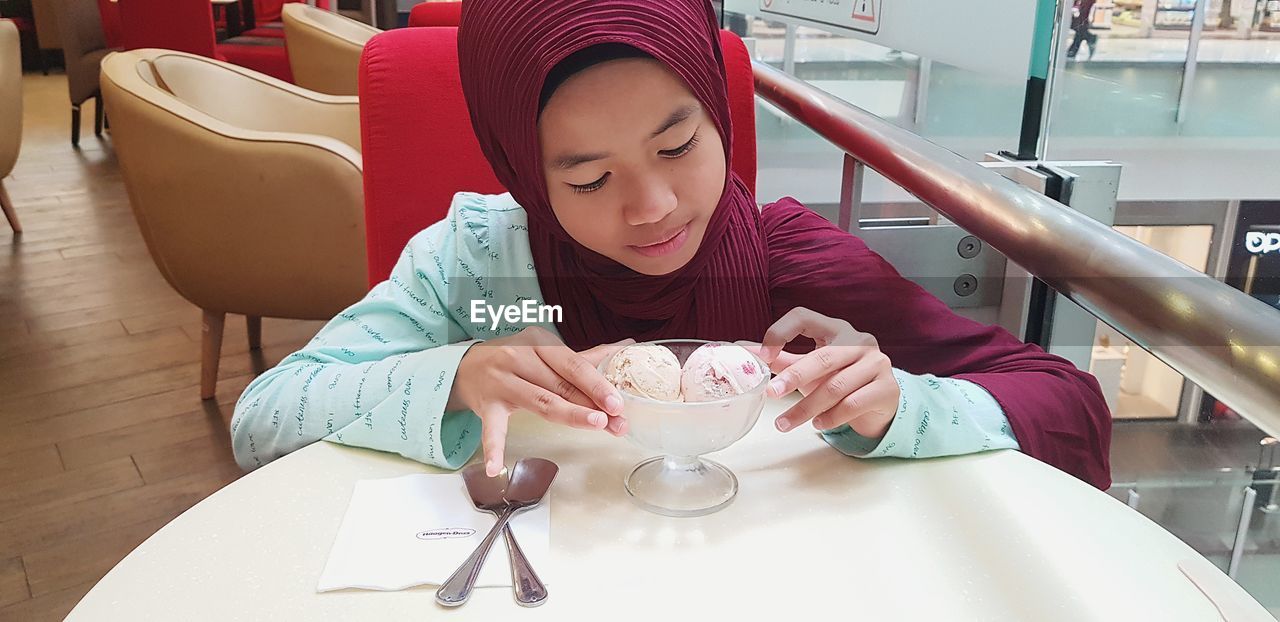 Girl in headscarf eating ice cream on table