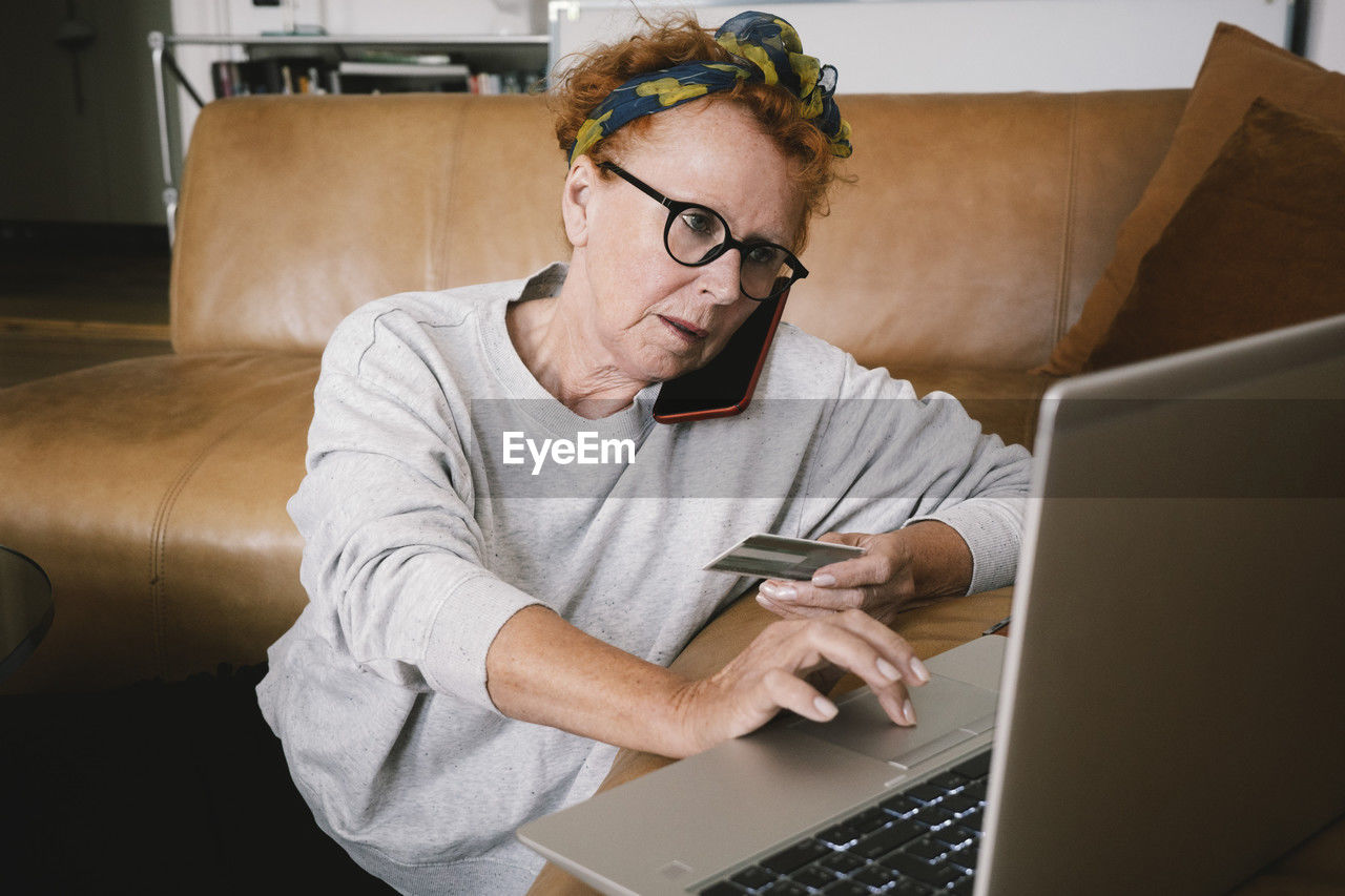Senior woman talking on smart phone while making online payment through laptop