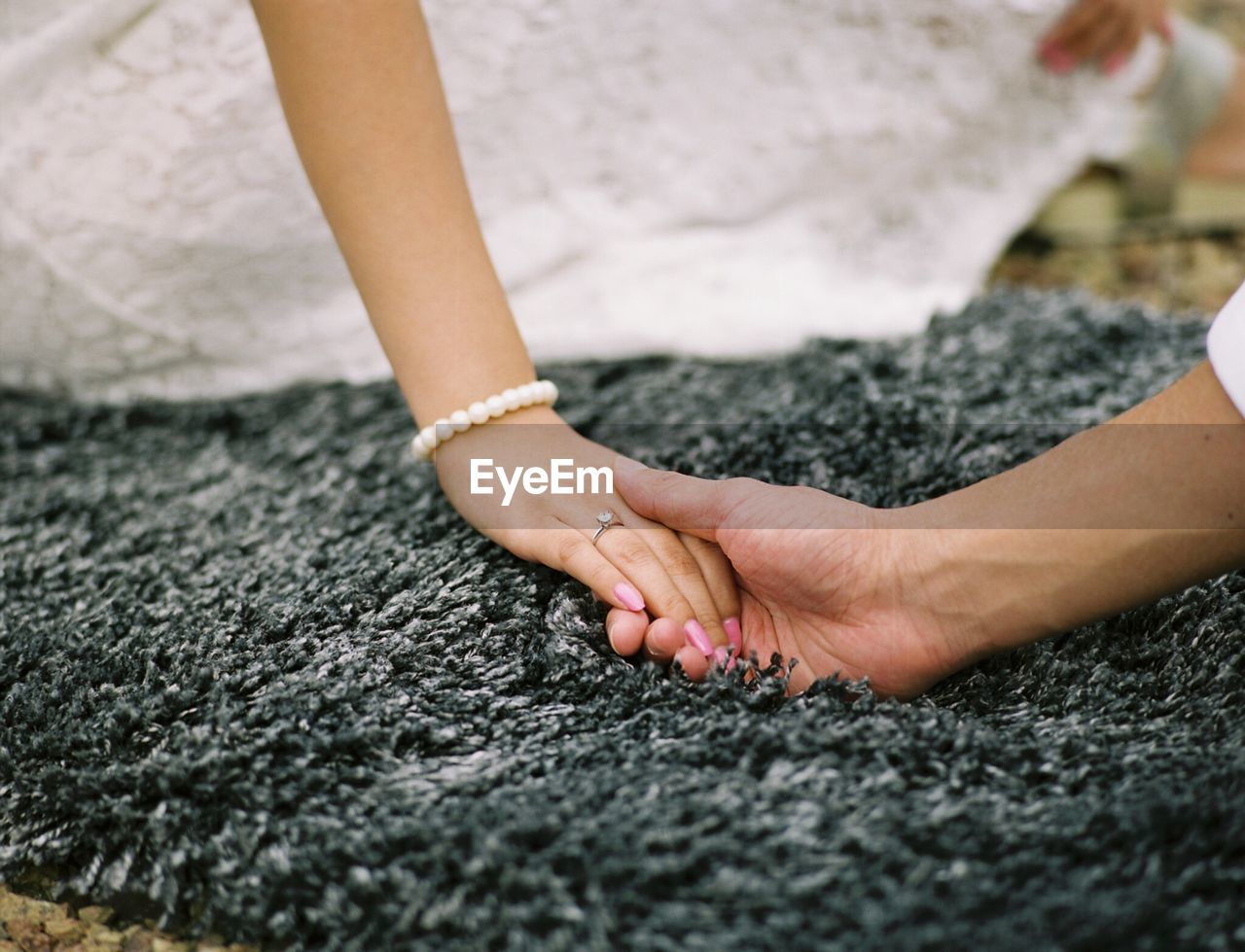 Cropped image of bridegroom holding hand of bride on carpet 