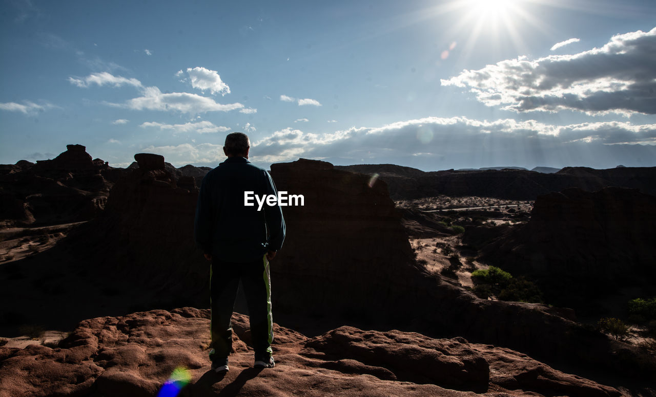 REAR VIEW OF MAN STANDING ON ROCK