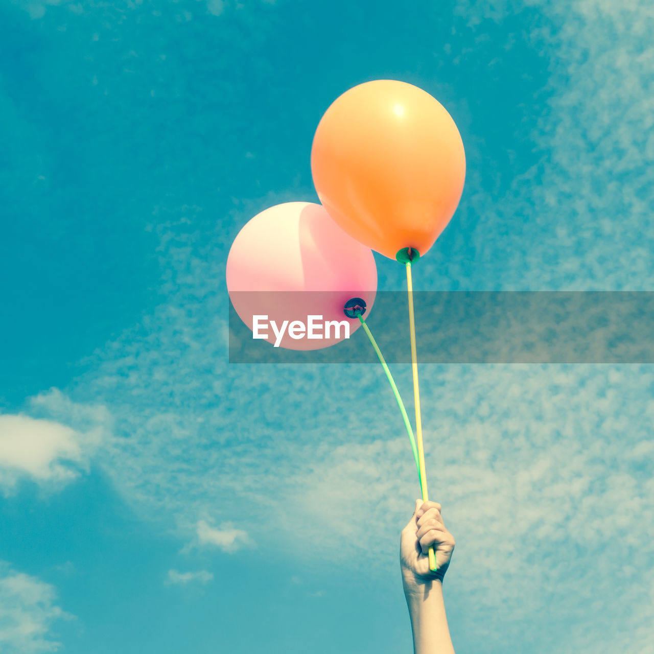 Cropped hand of child holding balloon against blue sky