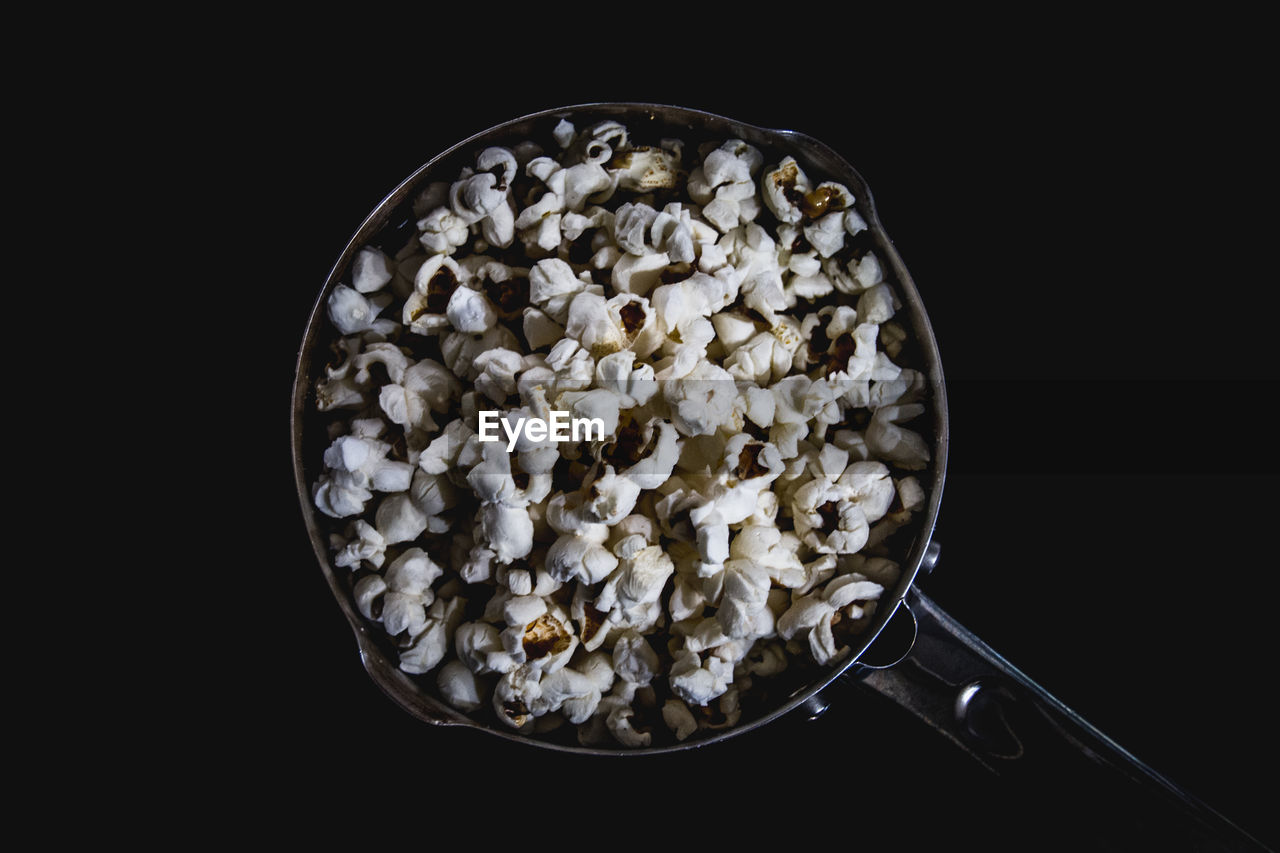 Directly above shot of popcorn in saucepan over black background