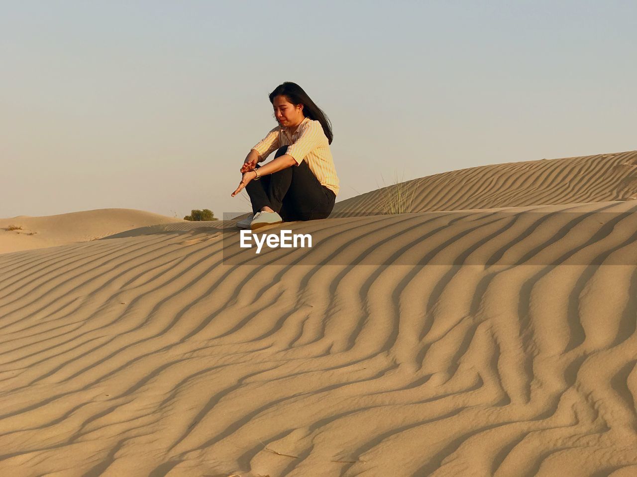 Woman sitting on sand dune in desert against clear sky