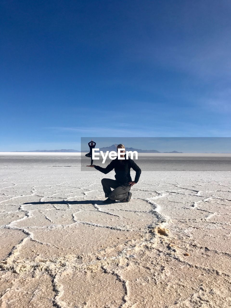 Digital composite image of woman holding man while kneeling on salt flat against blue sky