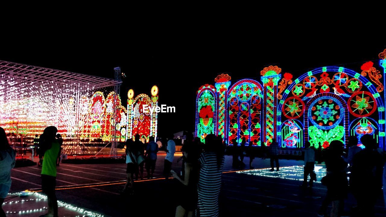 GROUP OF PEOPLE AGAINST ILLUMINATED LIGHTS