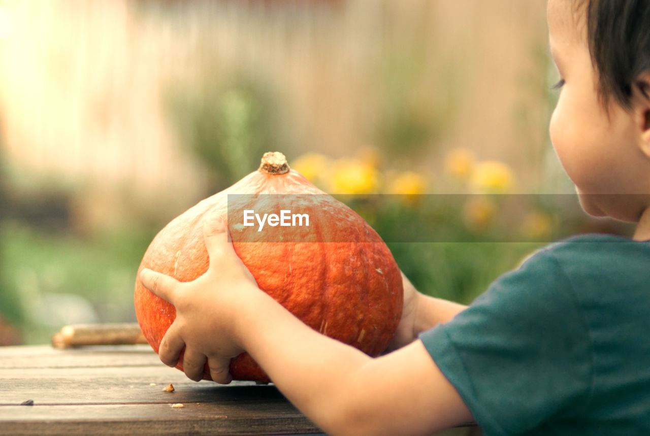 Side view of boy holding pumpkin on table