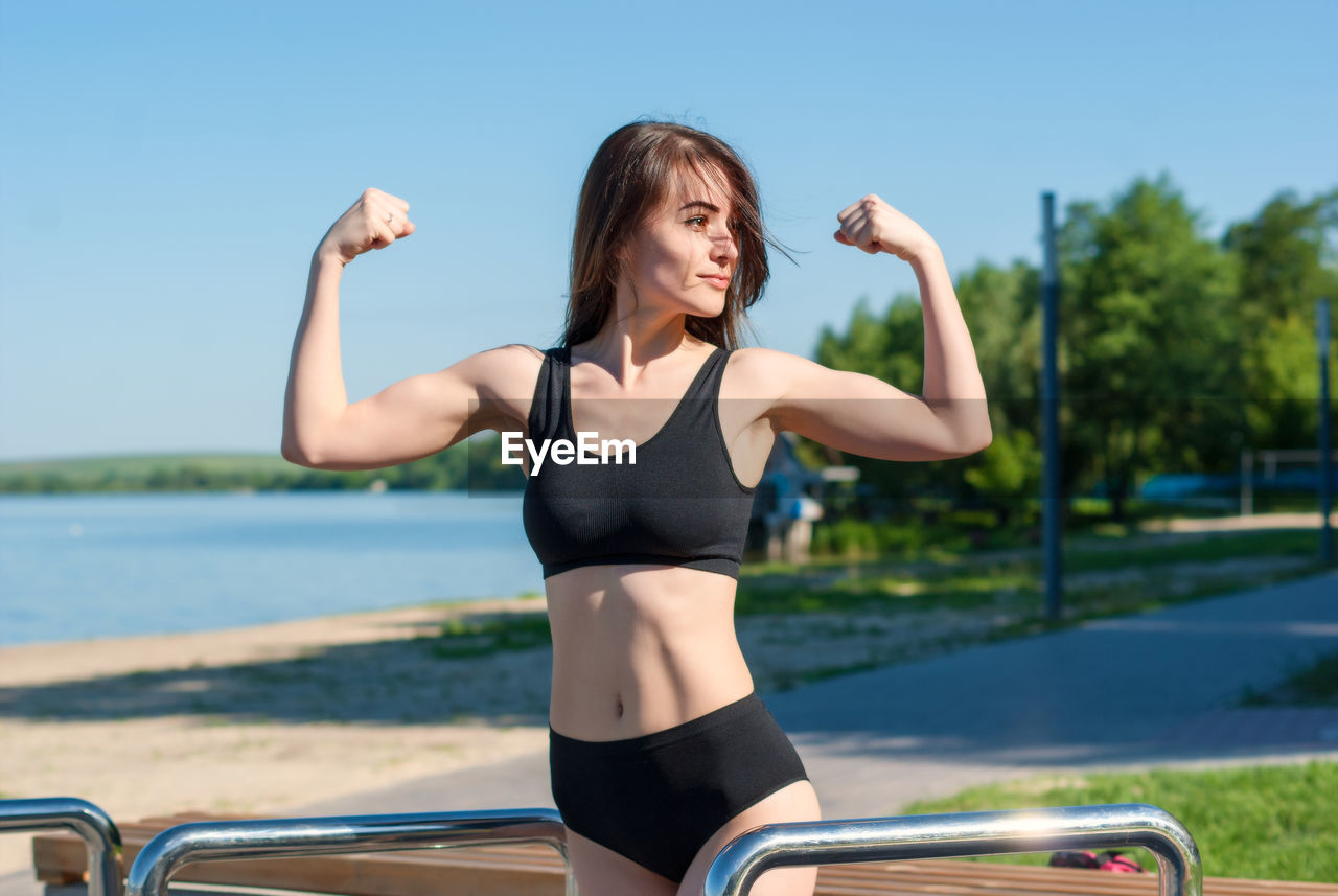 YOUNG WOMAN WITH ARMS OUTSTRETCHED AGAINST SKY