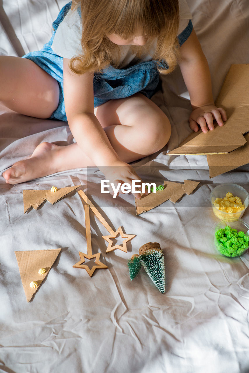 High angle view of girl playing with decoration while sitting on bed