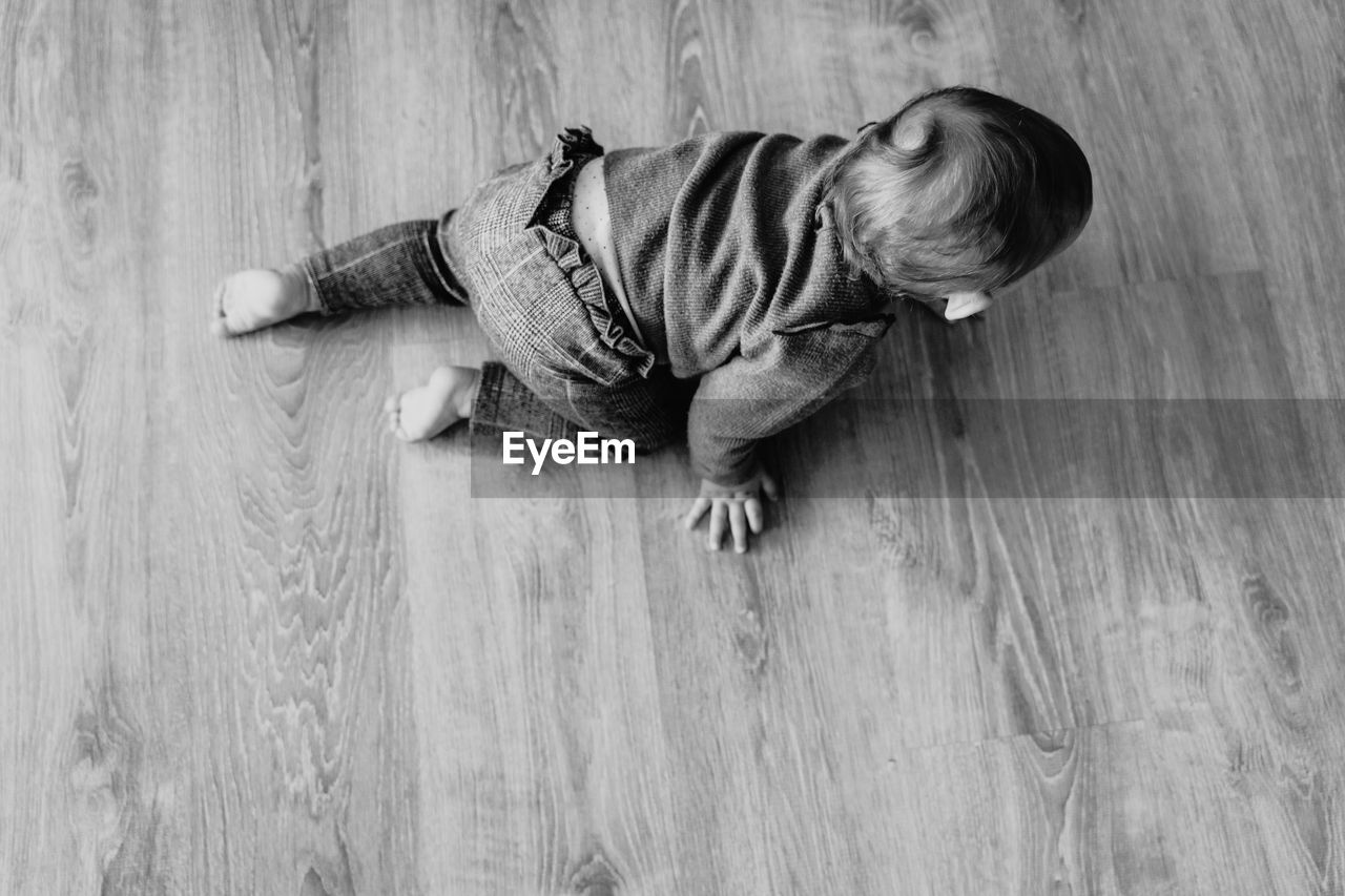 High angle view of baby girl crawling on hardwood floor