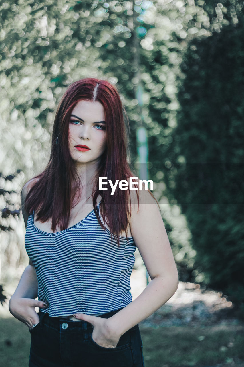 Portrait of beautiful woman standing against trees