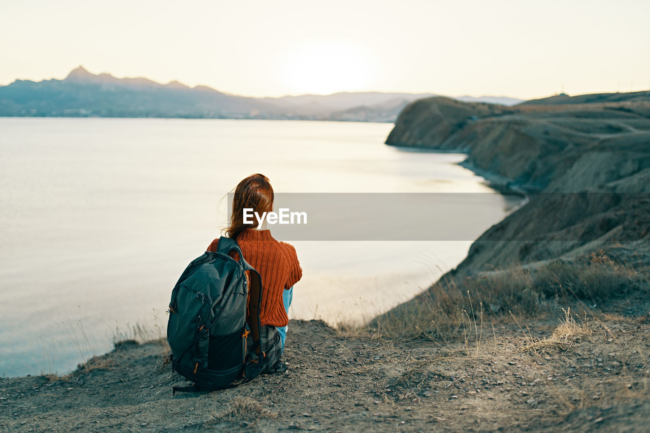 REAR VIEW OF WOMAN SITTING ON SHORE