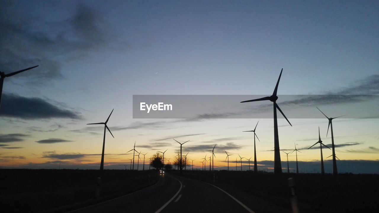 WINDMILLS ON ROAD AGAINST SKY DURING SUNSET
