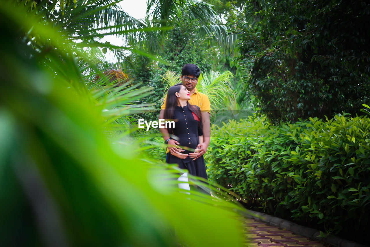 Young man with pregnant woman amidst plants