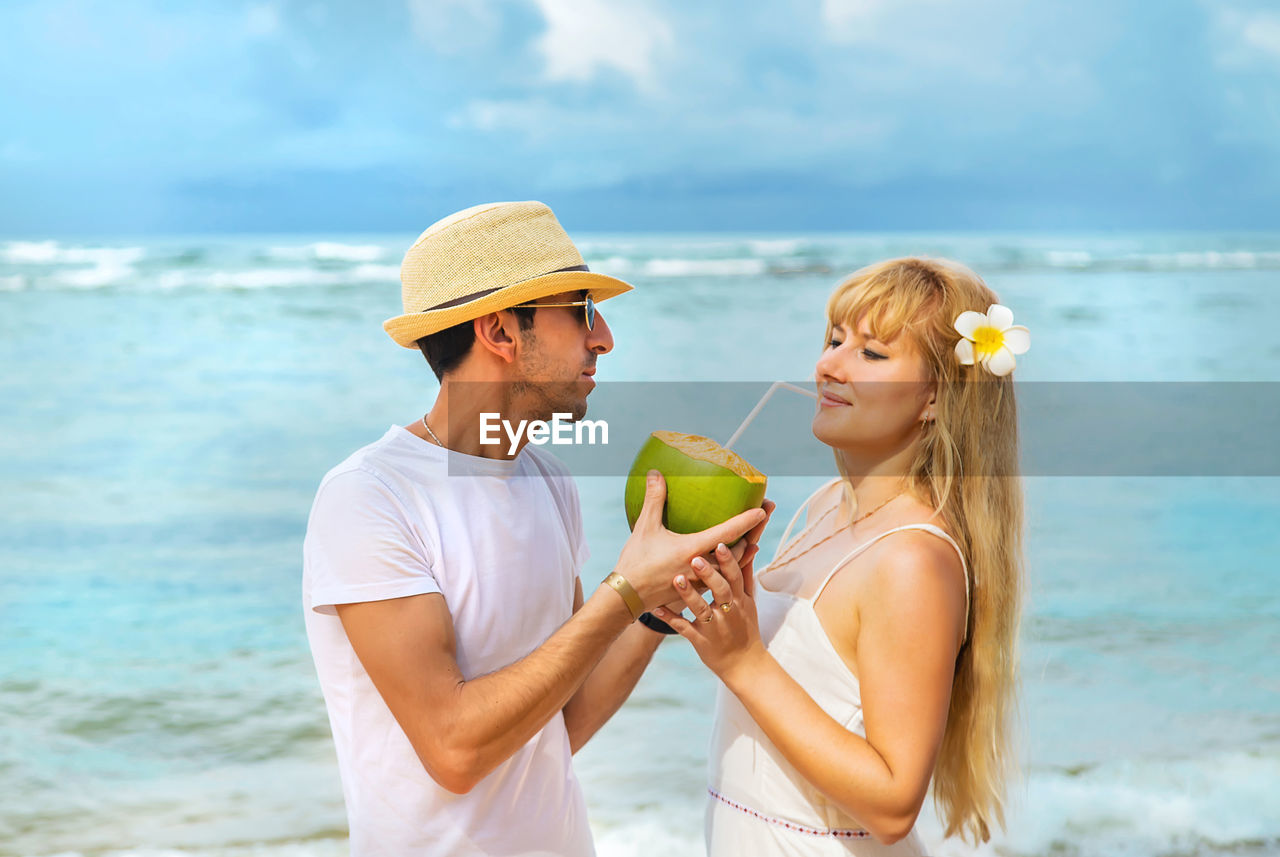 Man feeding coconut water to woman at beach