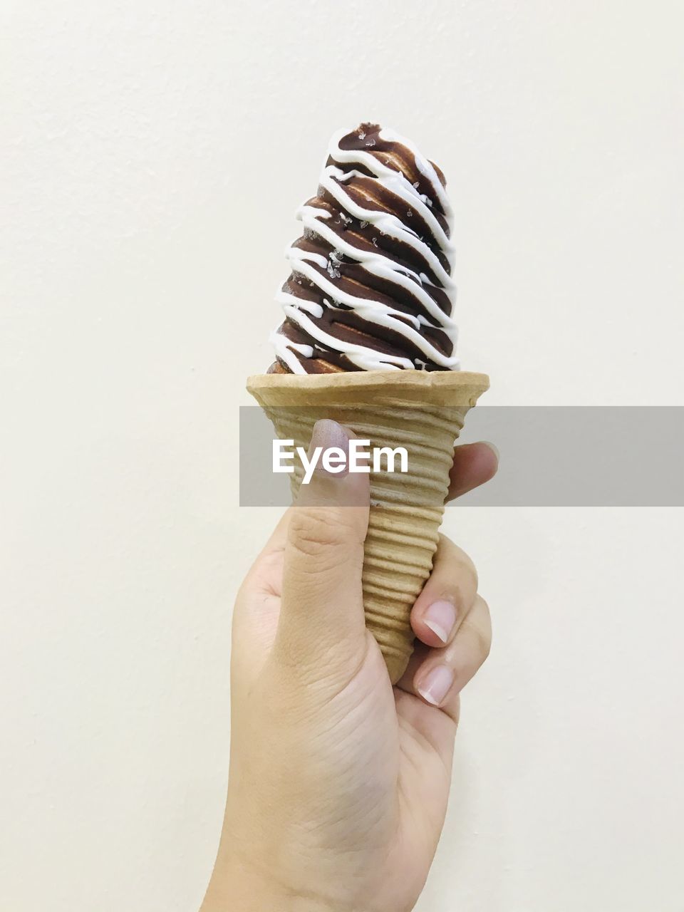 HAND HOLDING ICE CREAM CONE AGAINST WHITE BACKGROUND