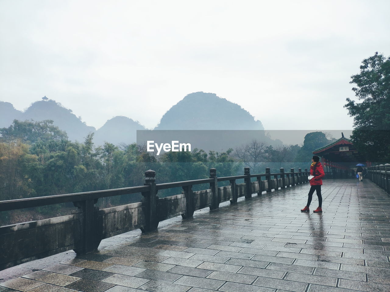 A girl standing on wet bridge looking at mountains in the mist