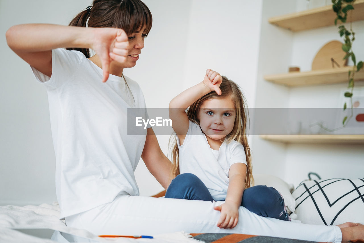 Woman looking at daughter showing thumbs down