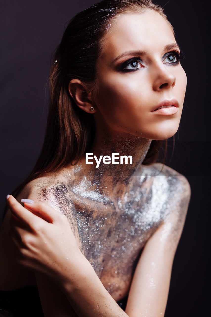 Shirtless young woman with silver glitter on her body against black background