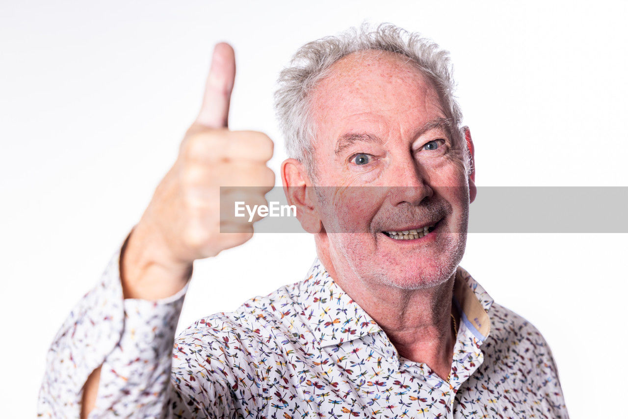 adult, portrait, one person, finger, person, men, senior adult, emotion, gesturing, smiling, human face, gray hair, hand, white background, studio shot, happiness, looking at camera, mature adult, cut out, seniors, thumbs up, positive emotion, indoors, hand sign, human head, headshot, cheerful, sign language, nose, casual clothing, front view, pointing, relaxation, clothing, communication, facial expression, retirement, arm, facial hair, white, human mouth