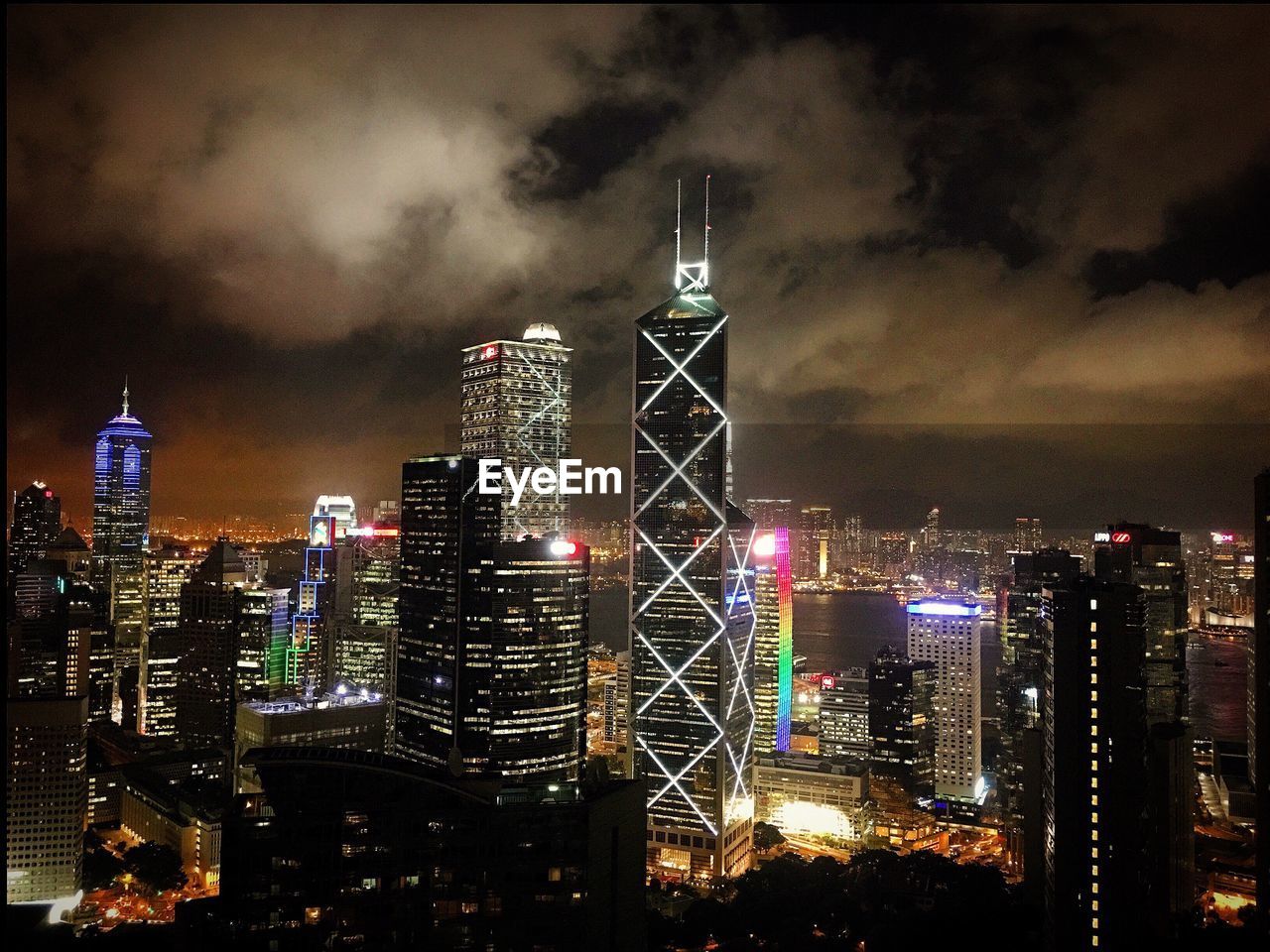 Illuminated cityscape against cloudy sky at night