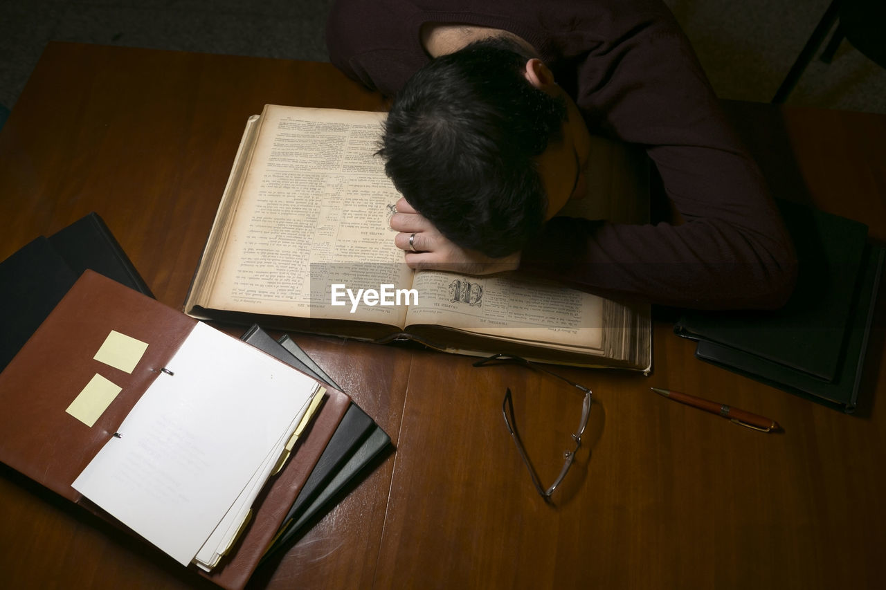 HIGH ANGLE VIEW OF MAN SITTING ON BOOK