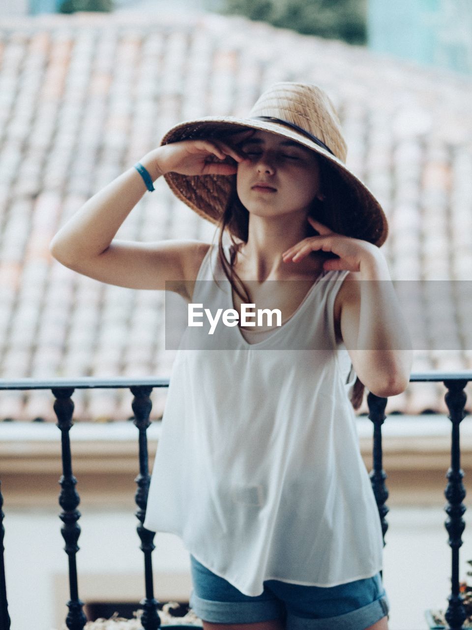 Young woman on the balcony wearing summer clothes and a hat