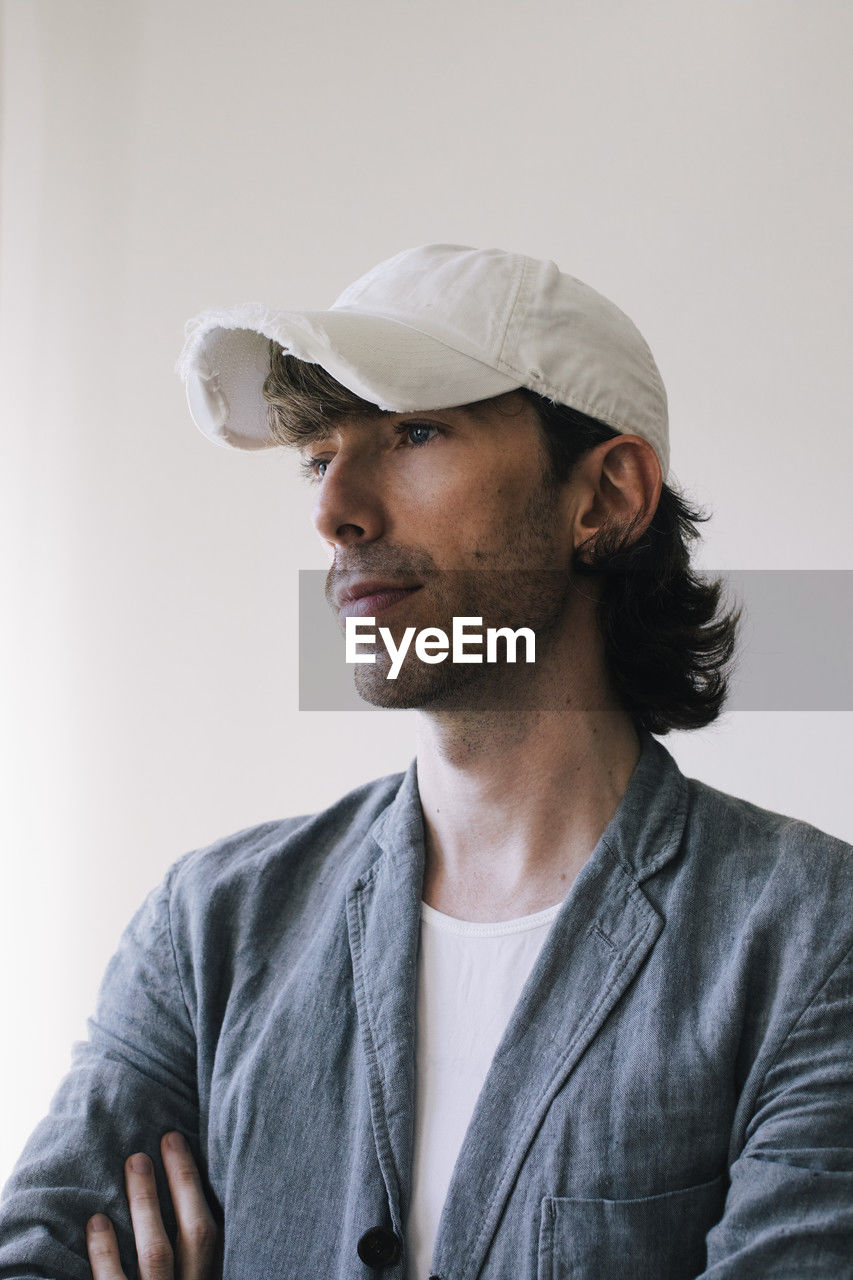 Thoughtful male architect wearing cap and blazer against white wall