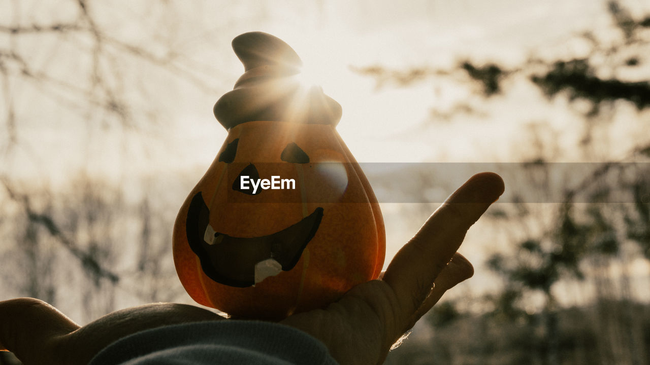 Cropped hand holding jack o lantern against sky during sunny day