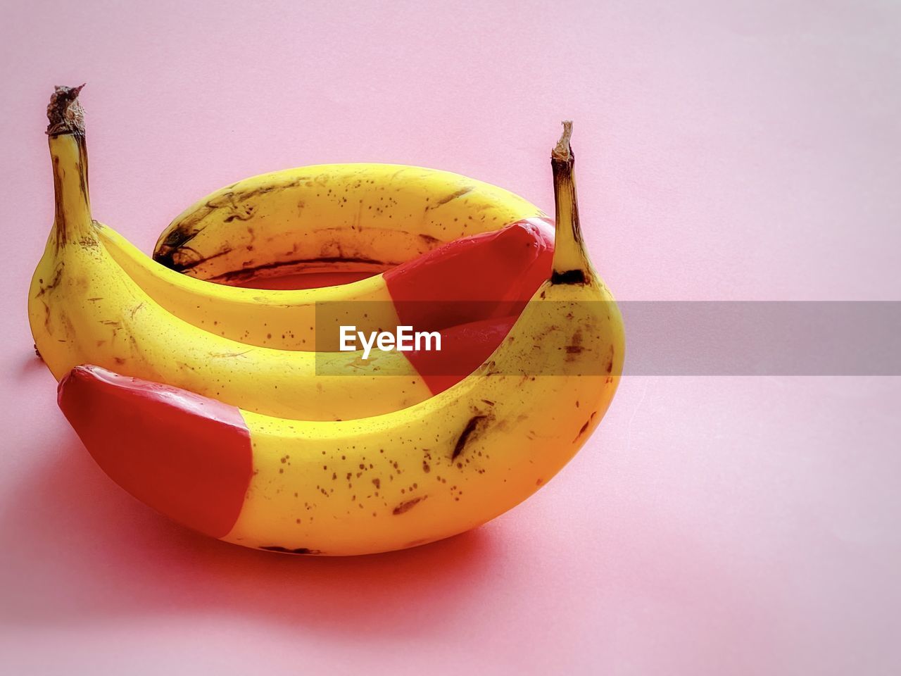 Close-up of red tipped bananas on pink background.