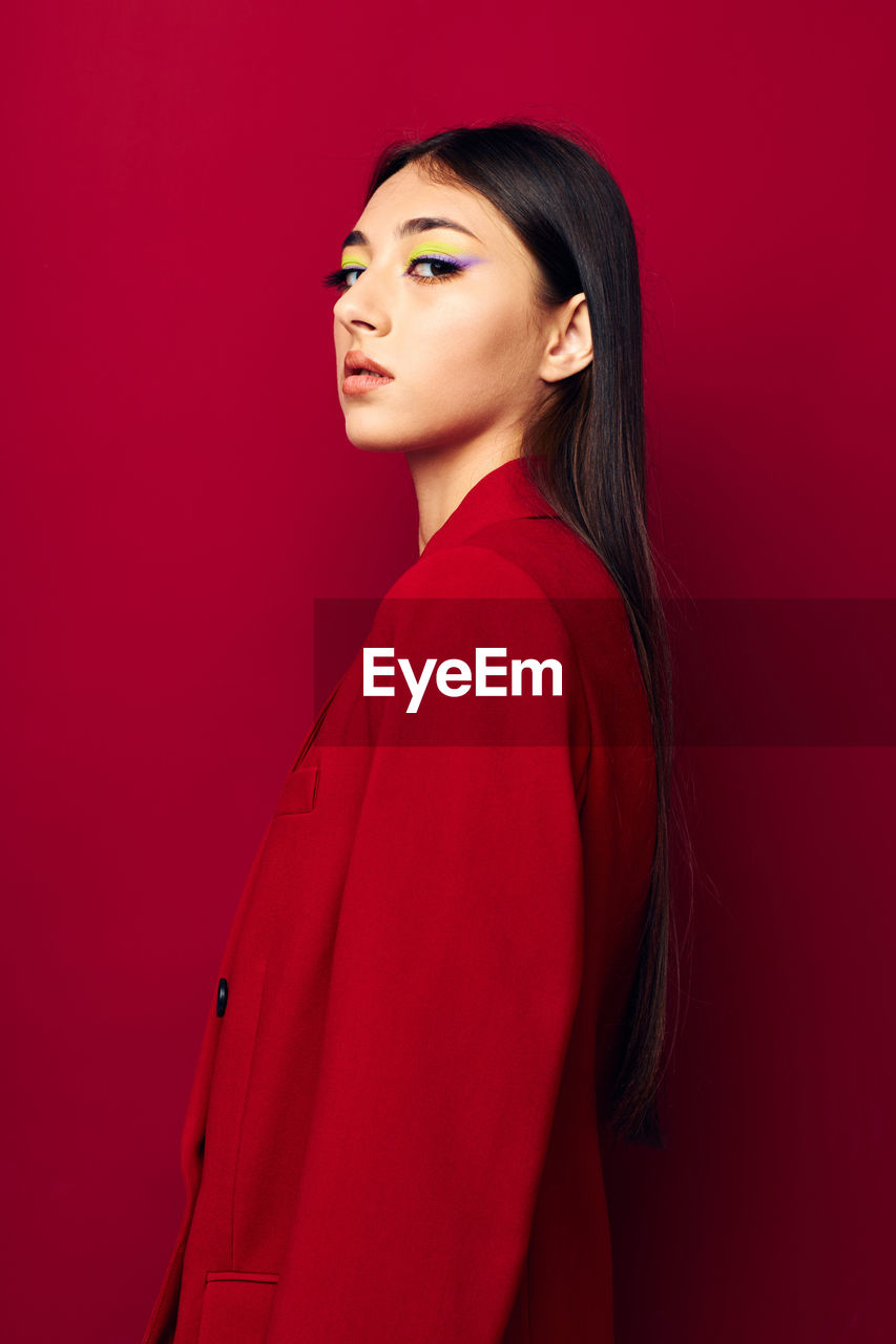 Portrait of young woman standing against red background