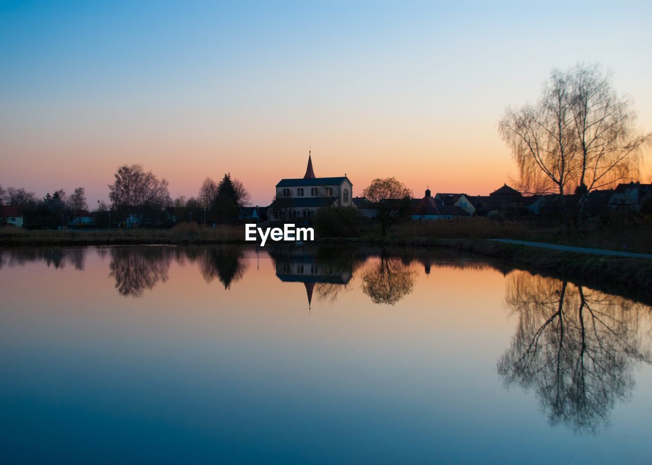 Scenic view of lake by buildings against sky during sunset