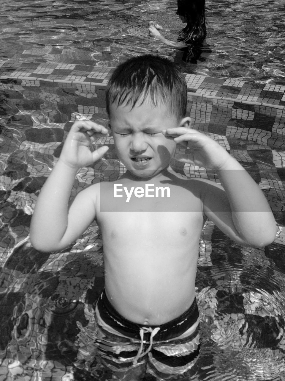 Shirtless boy with closed eyes standing in swimming pool
