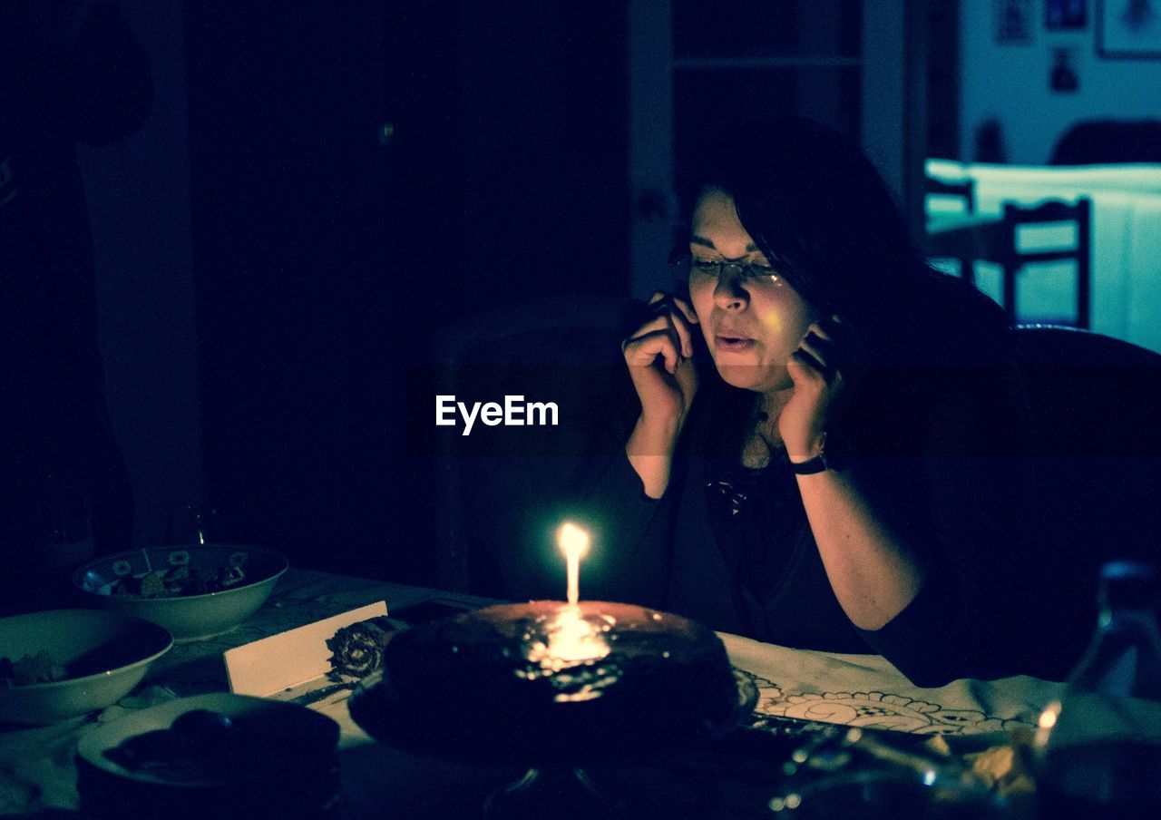 Woman blowing candle on cake in darkroom at home