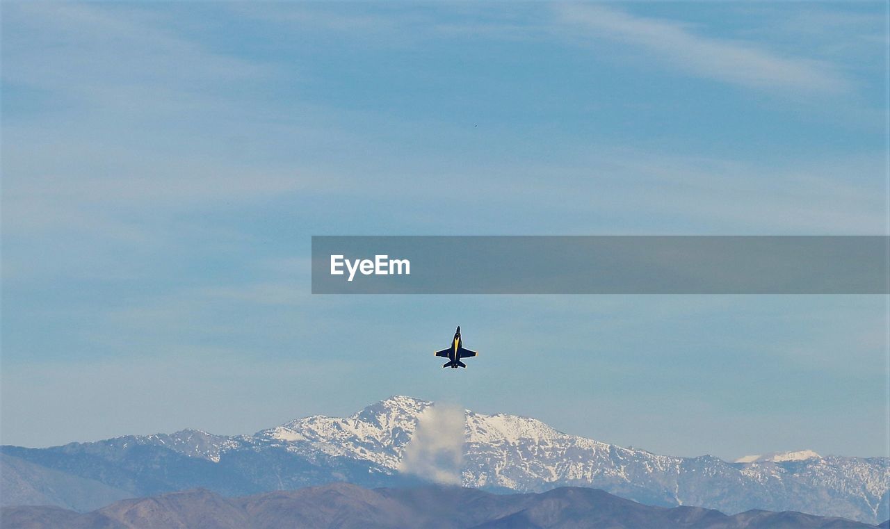 LOW ANGLE VIEW OF AIRPLANE FLYING OVER MOUNTAINS AGAINST SKY
