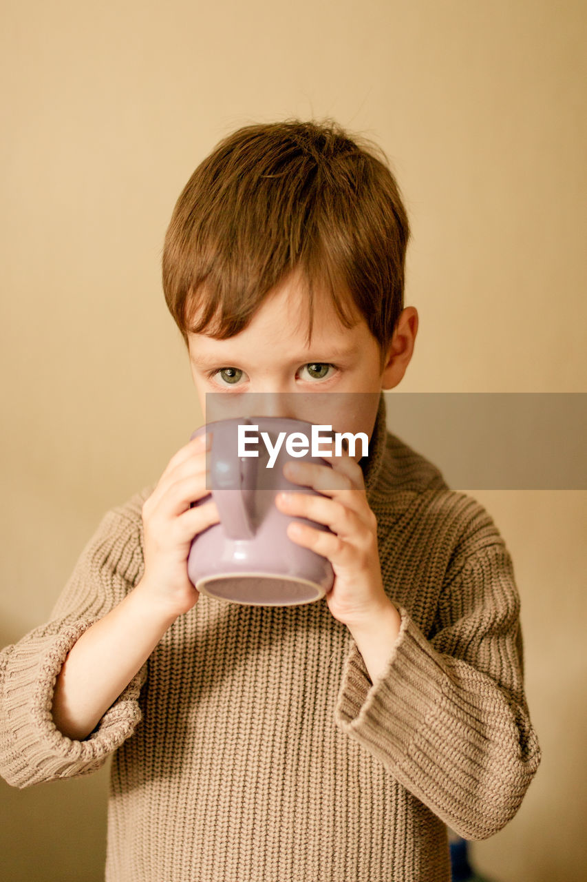 Boy drinks cocoa. warm autumn photography. a boy in a brown sweater drinks from a mug.