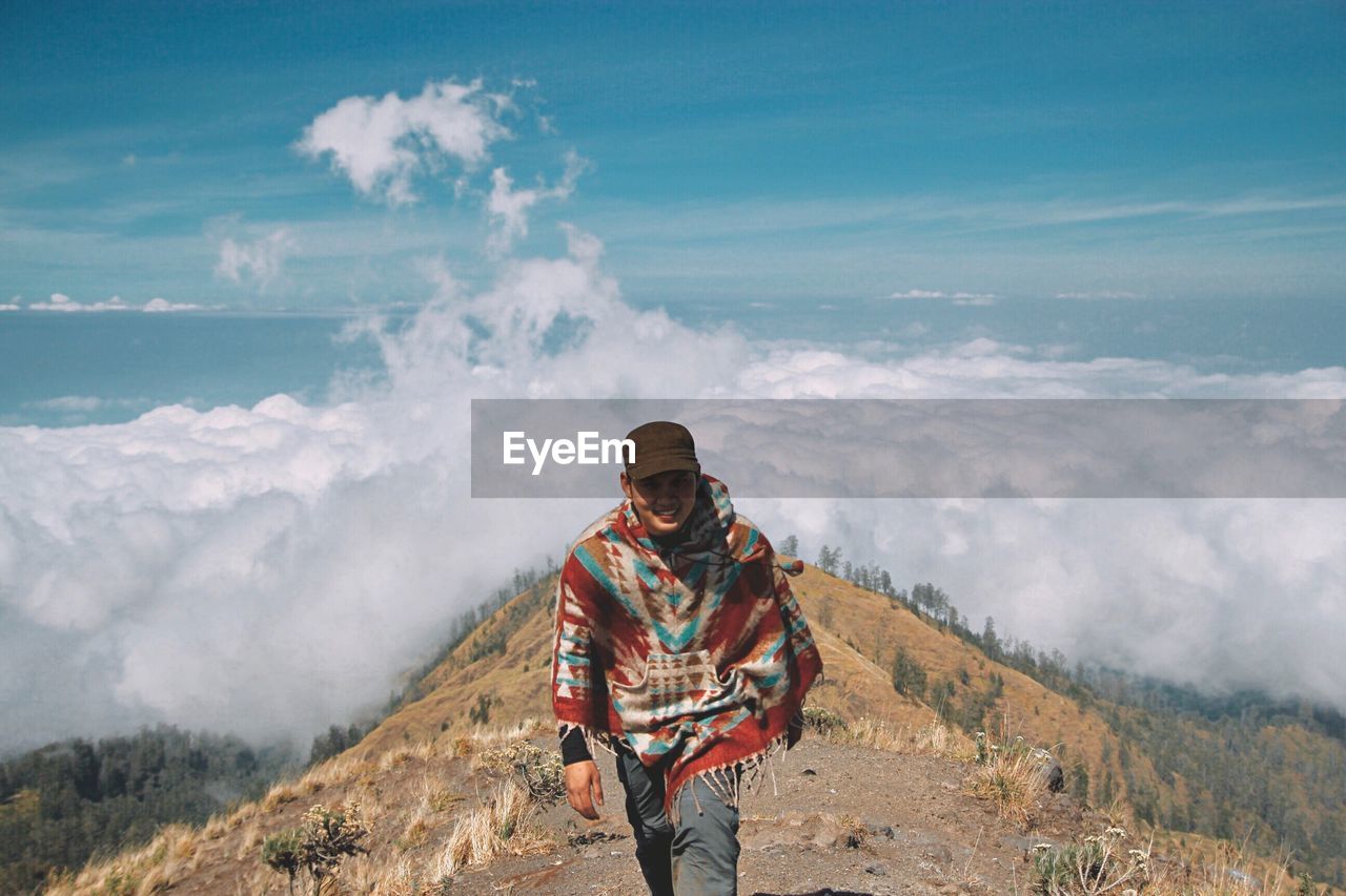 Portrait of young man hiking on mountain against cloudscape