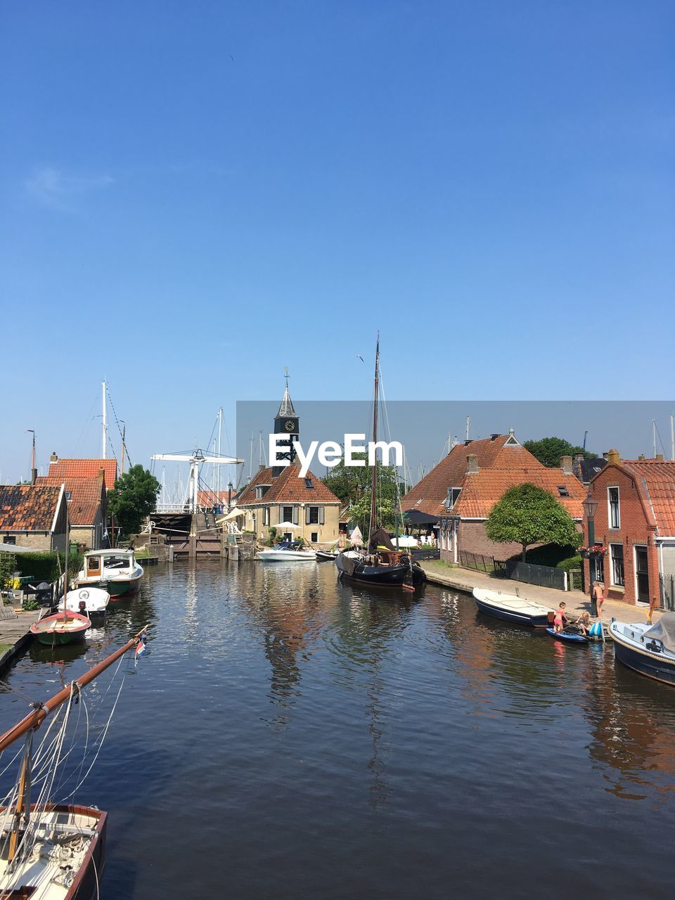 Sailboats moored on river by buildings against clear blue sky