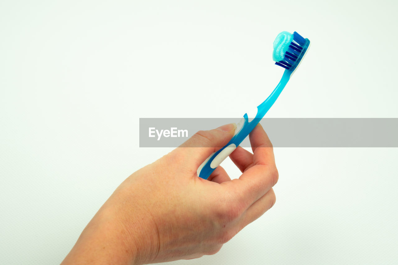 Midsection of person holding toothbrush with toothpaste against white background