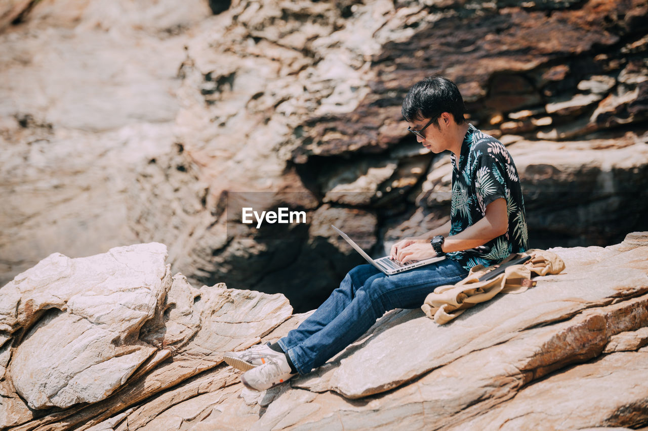 Man using laptop while sitting on rock