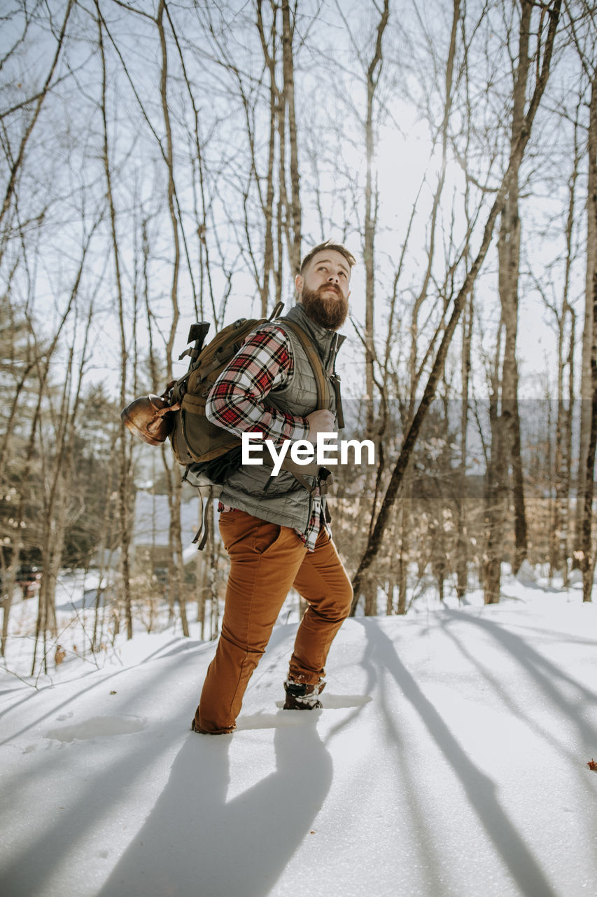 Man with beard wearing flannel hikes through snow in maine woods