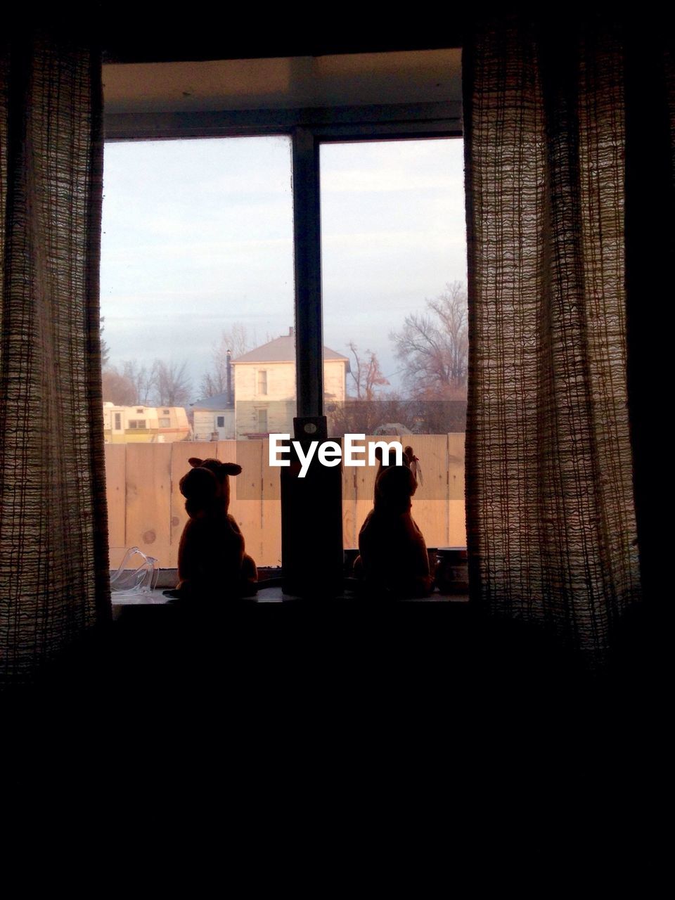 Silhouette stuffed toys on window sill against built structure