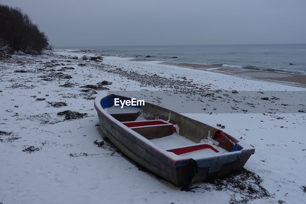 BOAT MOORED ON SHORE DURING WINTER