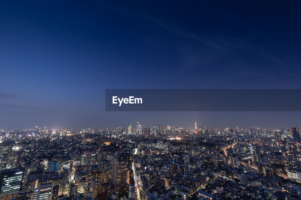 High angle view of city lit up against blue sky