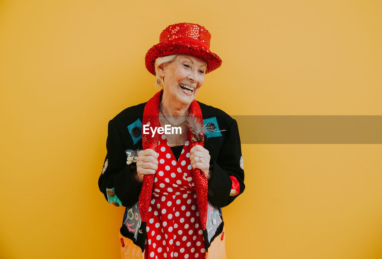 Smiling woman looking away while standing against yellow background