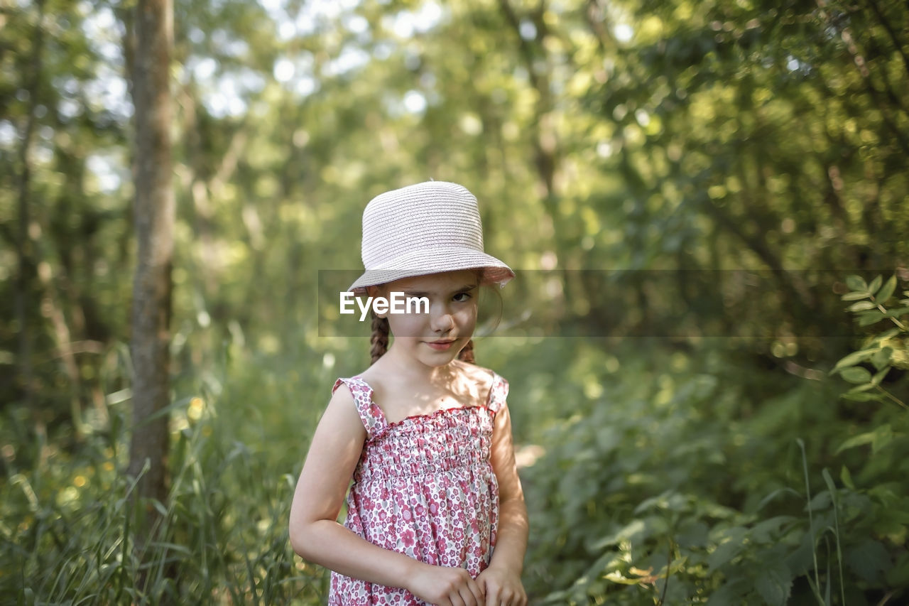 Portrait of cute girl wearing hat standing against trees