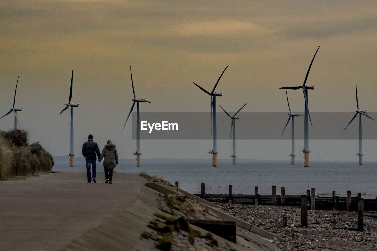 Rear view of couple walking on pier against sky during sunset