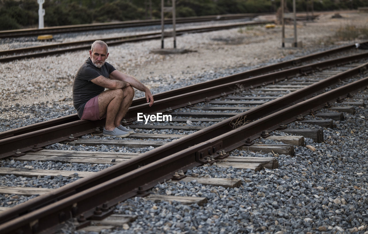 Portrait of man sitting on railroad track in summer